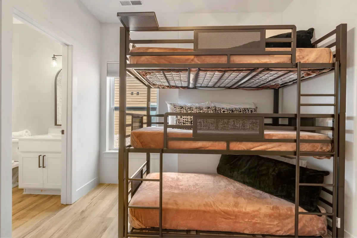 The room features sturdy bunk beds with textured bedding, a bathroom doorway visible in the background, and a lively, youthful ambiance. It’s designed for children or teens, with playful touches and a layout that ensures convenience and privacy.