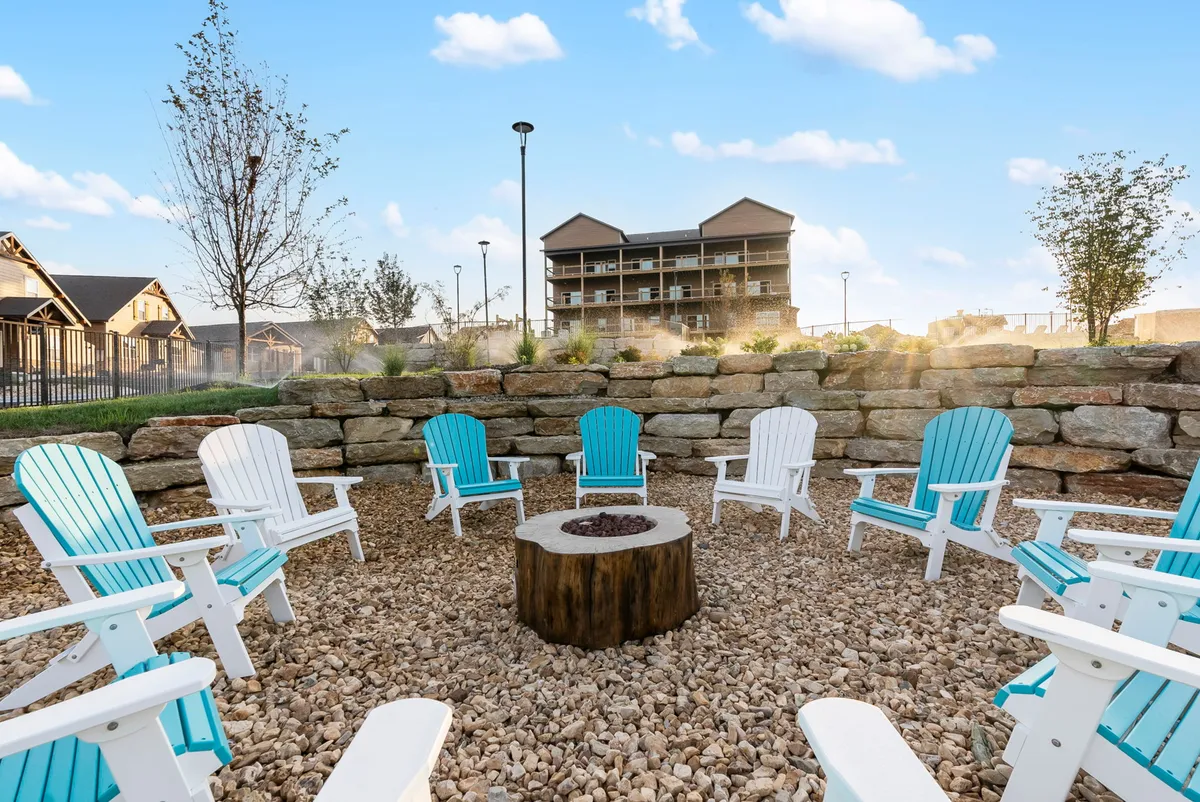 This exterior scene captures a communal fire pit encircled by Adirondack chairs, set against a backdrop of lush greenery. The gathering area looks inviting for evening socialization, storytelling, and roasting marshmallows as dusk falls.