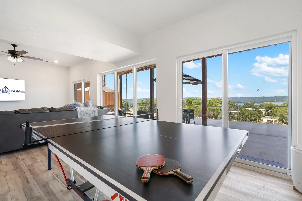 The image captures a spacious interior living area with a ping pong table, large windows that offer scenic views, and a cozy seating area. The space is lit with natural light and invites social gatherings and friendly competitions.