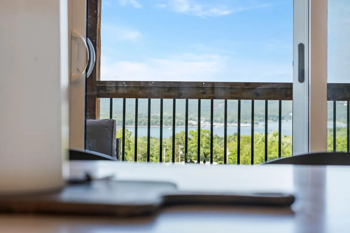 A peaceful balcony scene overlooking the lake, with a railing in the foreground and a mountain backdrop. Someone could be enjoying coffee or reading, with the calm water and sky offering a sense of relaxation after a day of adventure.