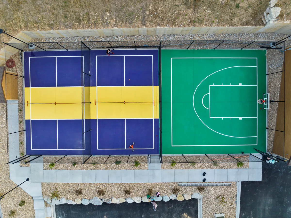 A dynamic exterior shot featuring dedicated tennis and basketball courts, with groups of players mid-action. The area is surrounded by well-maintained greenery, showcasing the resort’s sports facilities and the energy of friendly competitions.