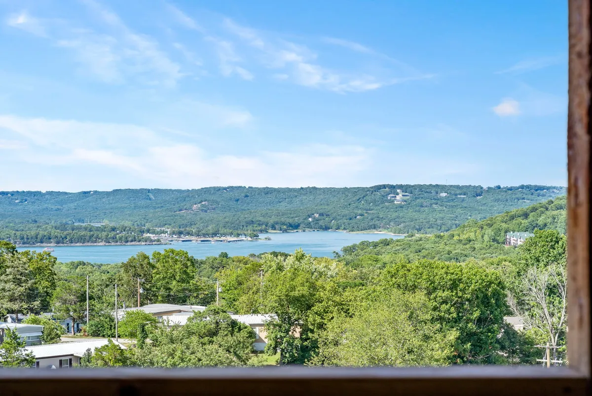 A wide panoramic view of Table Rock Lake surrounded by lush green trees and distant mountains beneath an open sky. The scene captures the tranquil water, inviting shoreline, and the natural beauty that defines the area. Activities like boating and fishing are visually implied by the expansive lake and serene atmosphere.