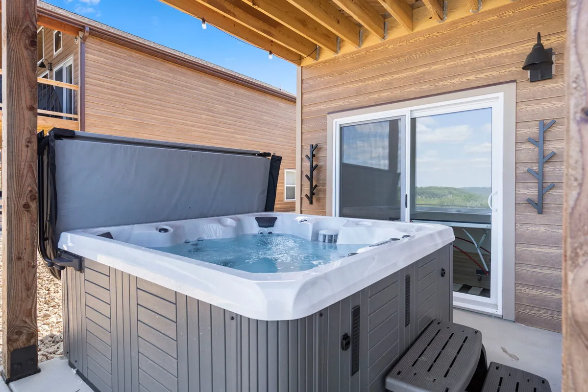 This image captures a tranquil outdoor hot tub area on a patio, surrounded by natural landscape. The inviting water, comfortable seating, and wide view of the outdoors set a relaxing and social atmosphere for both day and evening enjoyment.