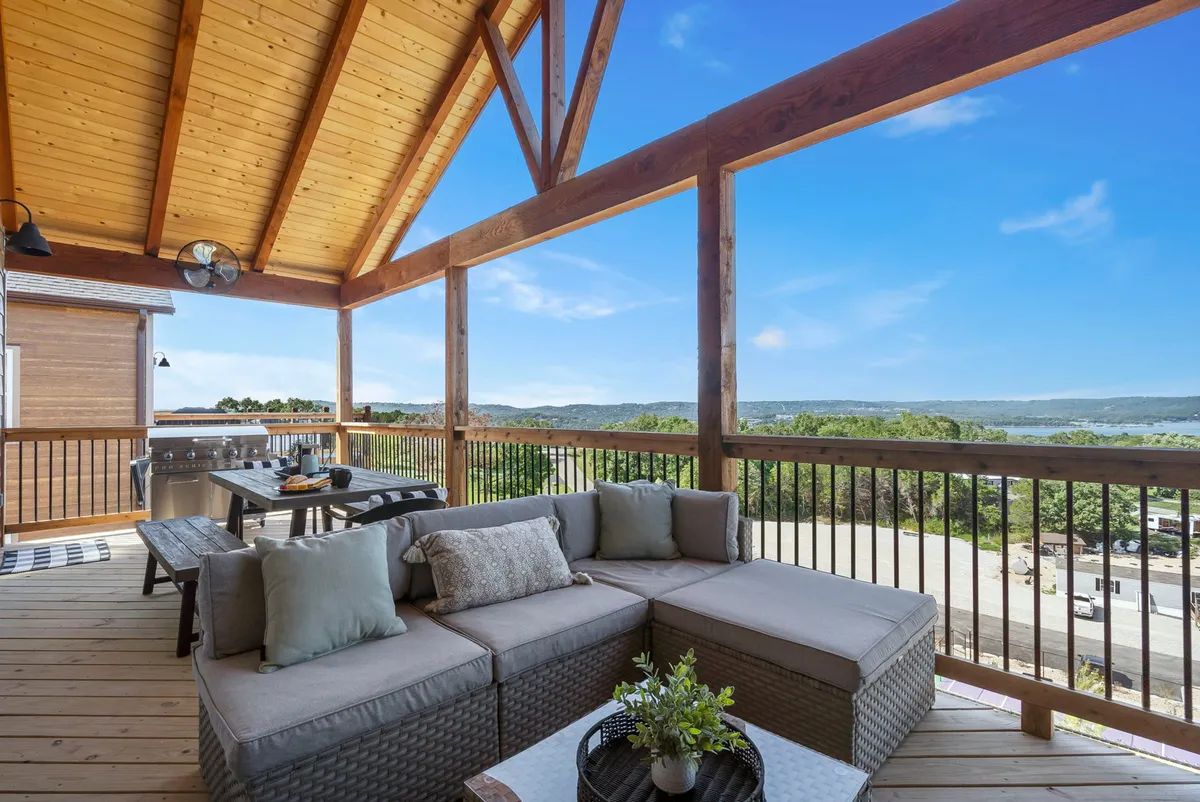 An inviting outdoor seating and dining area set on a deck, overlooking a scenic landscape. A spacious dining table anchors the area, surrounded by comfortable chairs, with the backdrop of nature and a gentle sunset glow enhancing the tranquil ambiance.