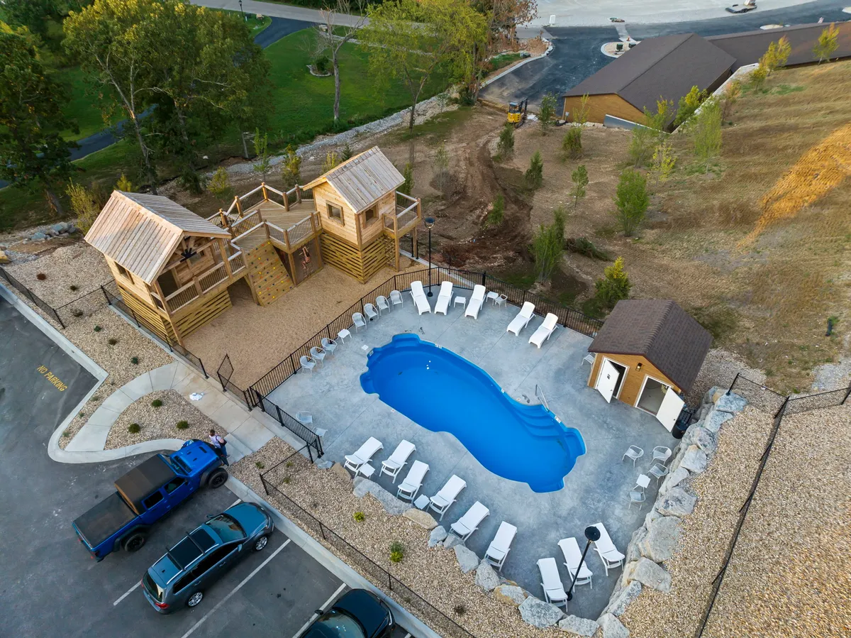 This exterior image showcases a sparkling swimming pool surrounded by lounge chairs and a prominent wooden play structure nearby. Children can be seen playing, and the setup is inviting for both sunbathing adults and playful kids. The relaxed, family-friendly atmosphere blends aquatic fun and imaginative outdoor play.