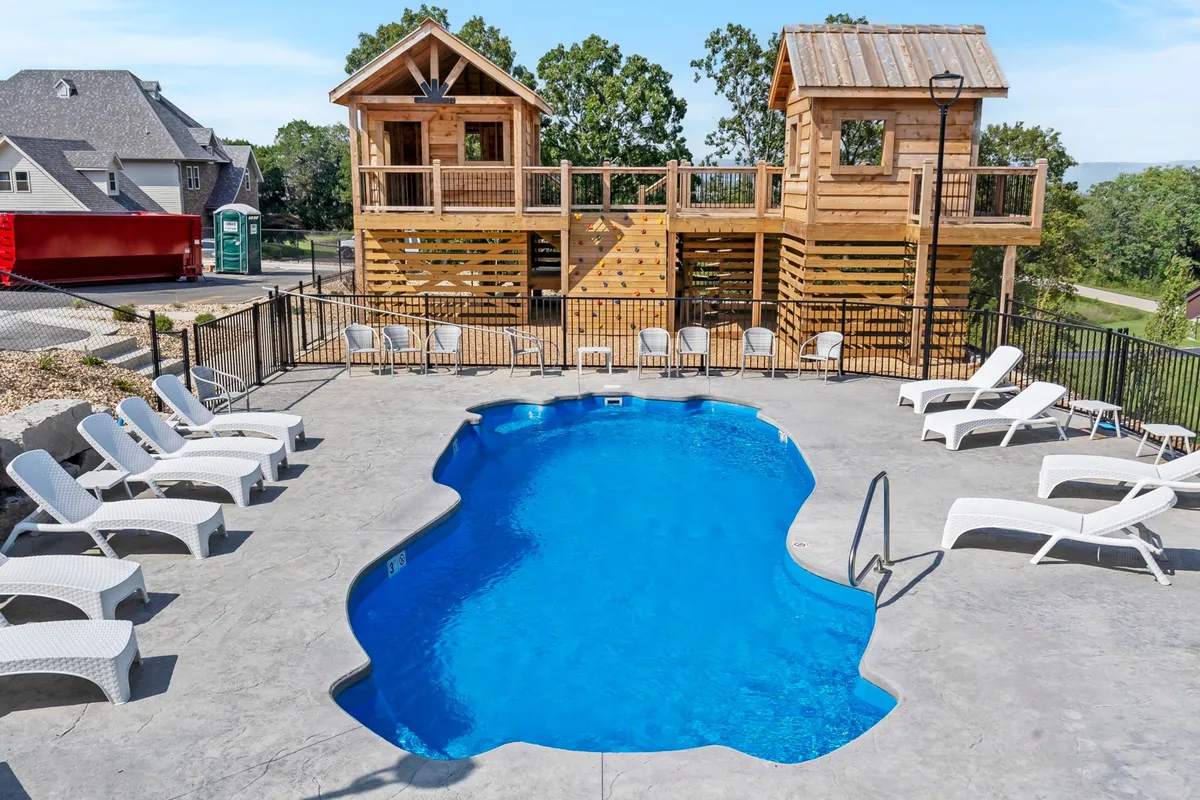 This exterior image features a sparkling swimming pool surrounded by lounge chairs, with wooden playhouses and a landscaped area nearby. The scene captures families enjoying sunny days by the pool and children engaging in outdoor play.